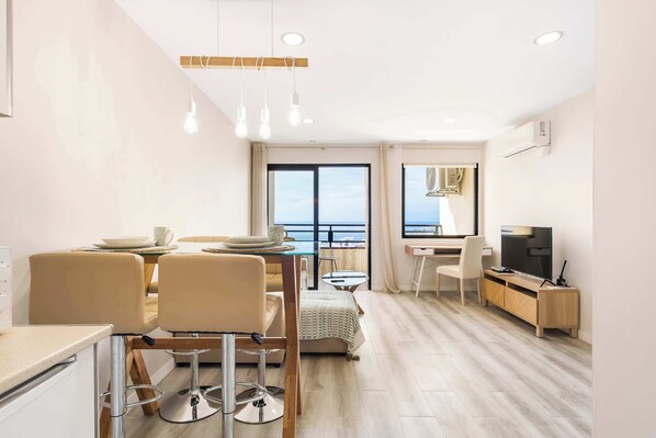 A modern living room with a dining area, a TV, and a view of the sea.