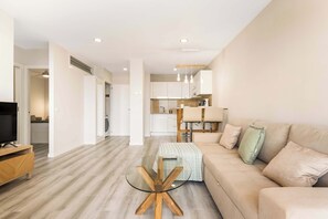 A modern living room with a glass coffee table, a beige sofa, and a TV on a wooden stand.