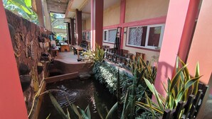 Un couloir intérieur étroit agrémenté d’un petit élément décoratif aquatique, de bancs en bois et de plantes en pot.
