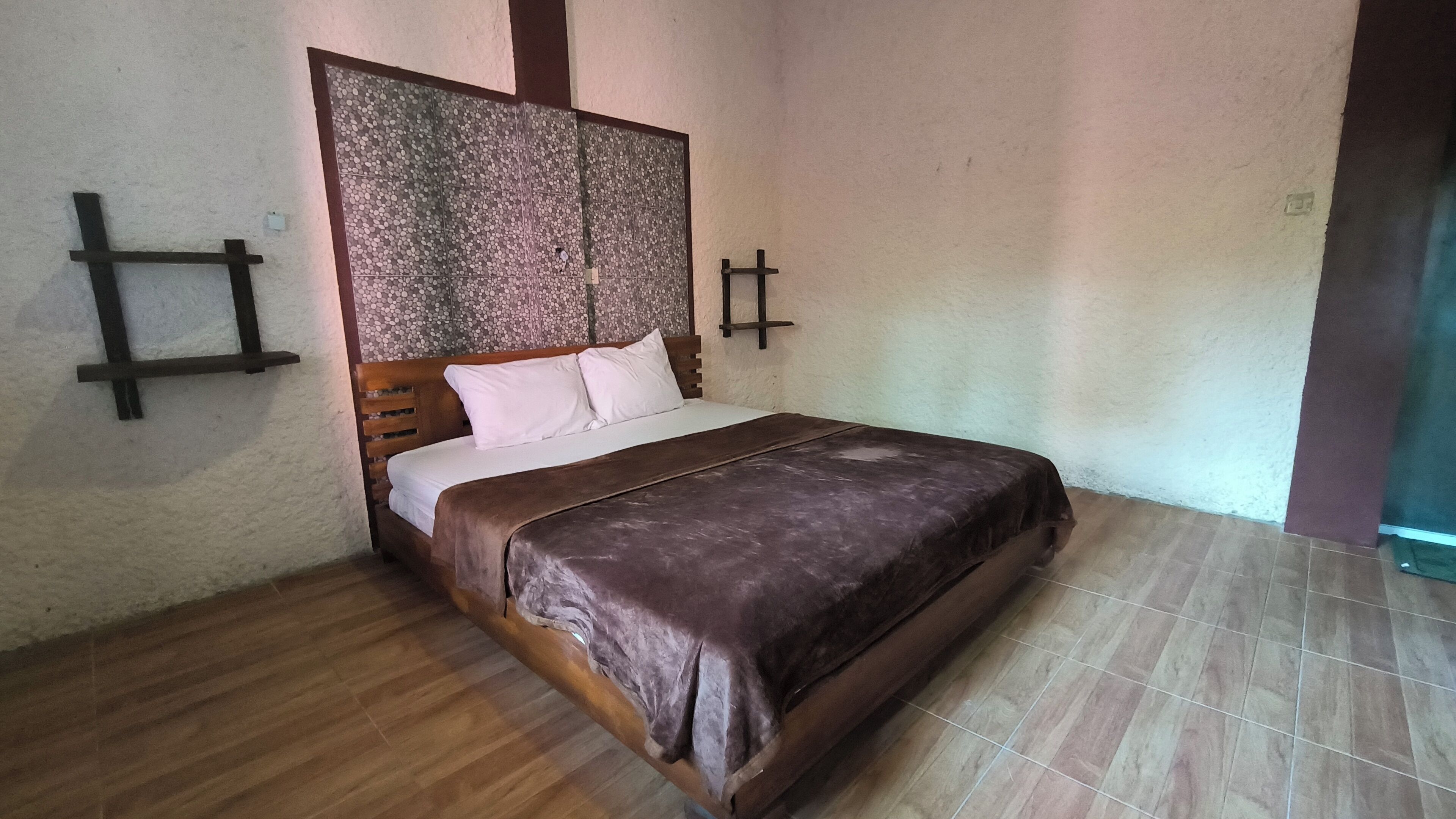 A bedroom with a wooden bed, white bedding, a patterned headboard, and a wooden floor.