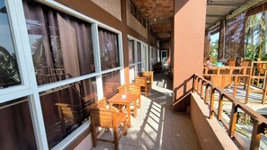 A covered outdoor seating area with wooden tables and chairs, large windows, and a view of the surrounding greenery. - New Lishafa Guesthouse (Karimun Jawa)