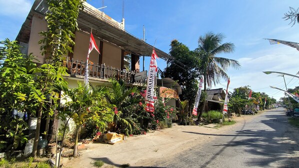 A hotel with a balcony, surrounded by tropical plants and flags. - New Lishafa Guesthouse (Karimun Jawa)