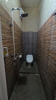 Baño pequeño y estrecho con inodoro, ducha y secador de manos. Las paredes están cubiertas de azulejos con diseño similar a la piedra.