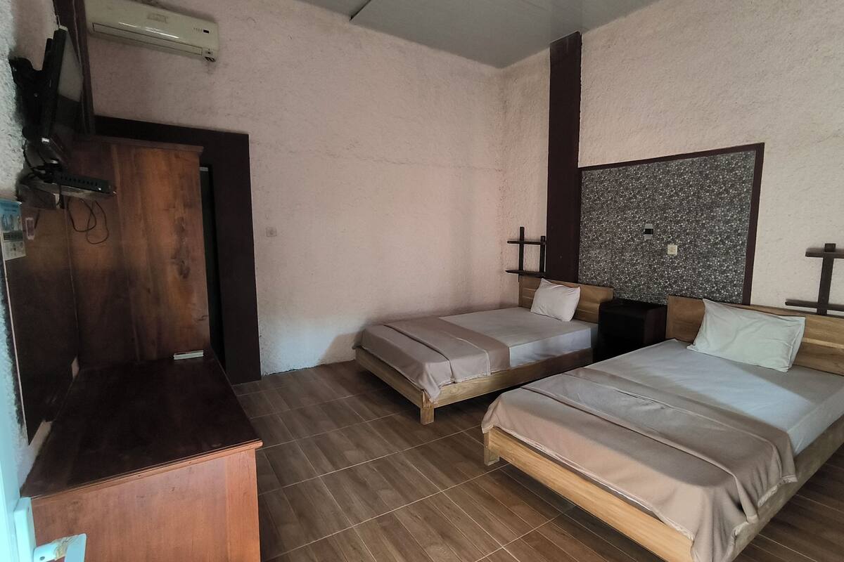 A room with two beds, a wooden desk, and a wall-mounted air conditioner.