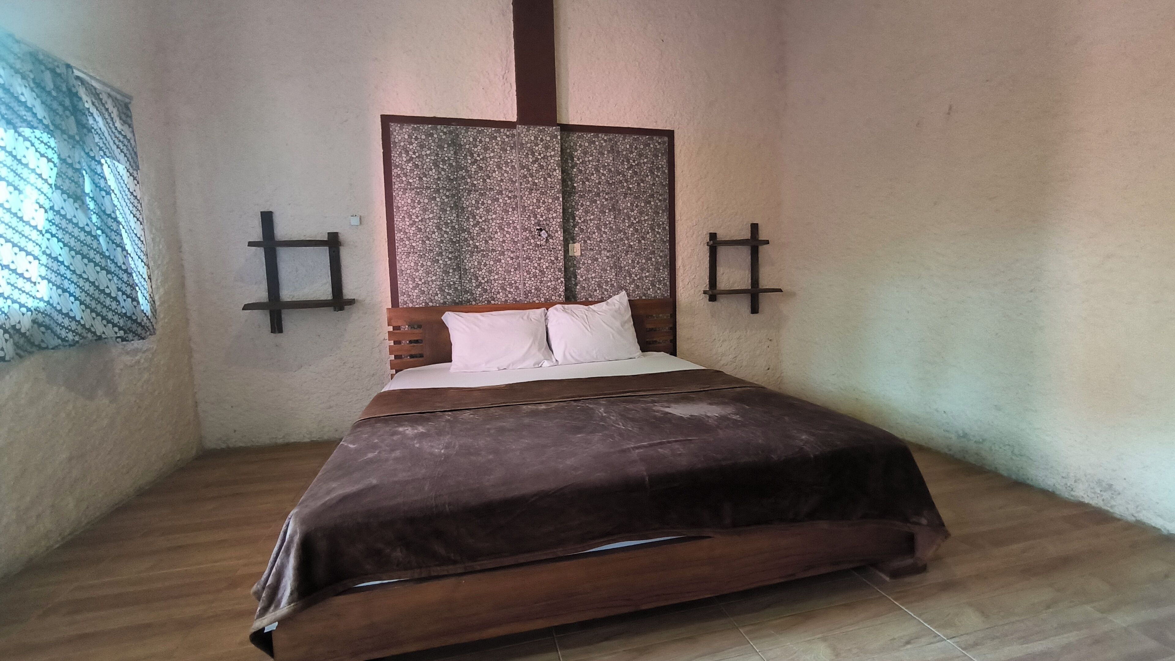 Un dormitorio con cama de madera, almohadas blancas, colcha marrón y cabecera decorativa.