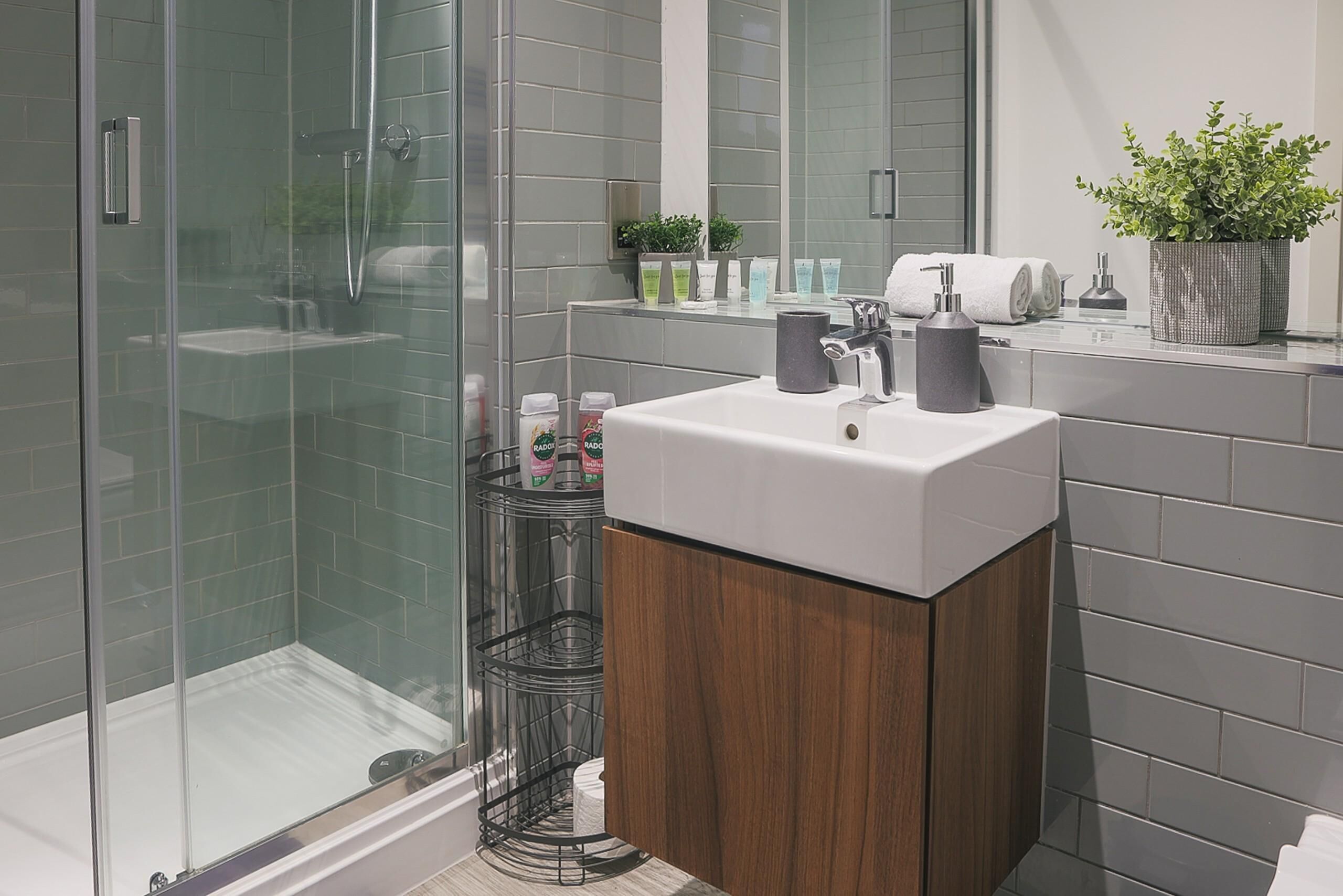 A modern bathroom with a glass-enclosed shower, a white sink, and a wooden vanity.