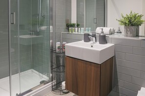 Ein modernes Badezimmer mit einer begehbaren Glasdusche, einem weißen Waschbecken und einer Holzausstattung.