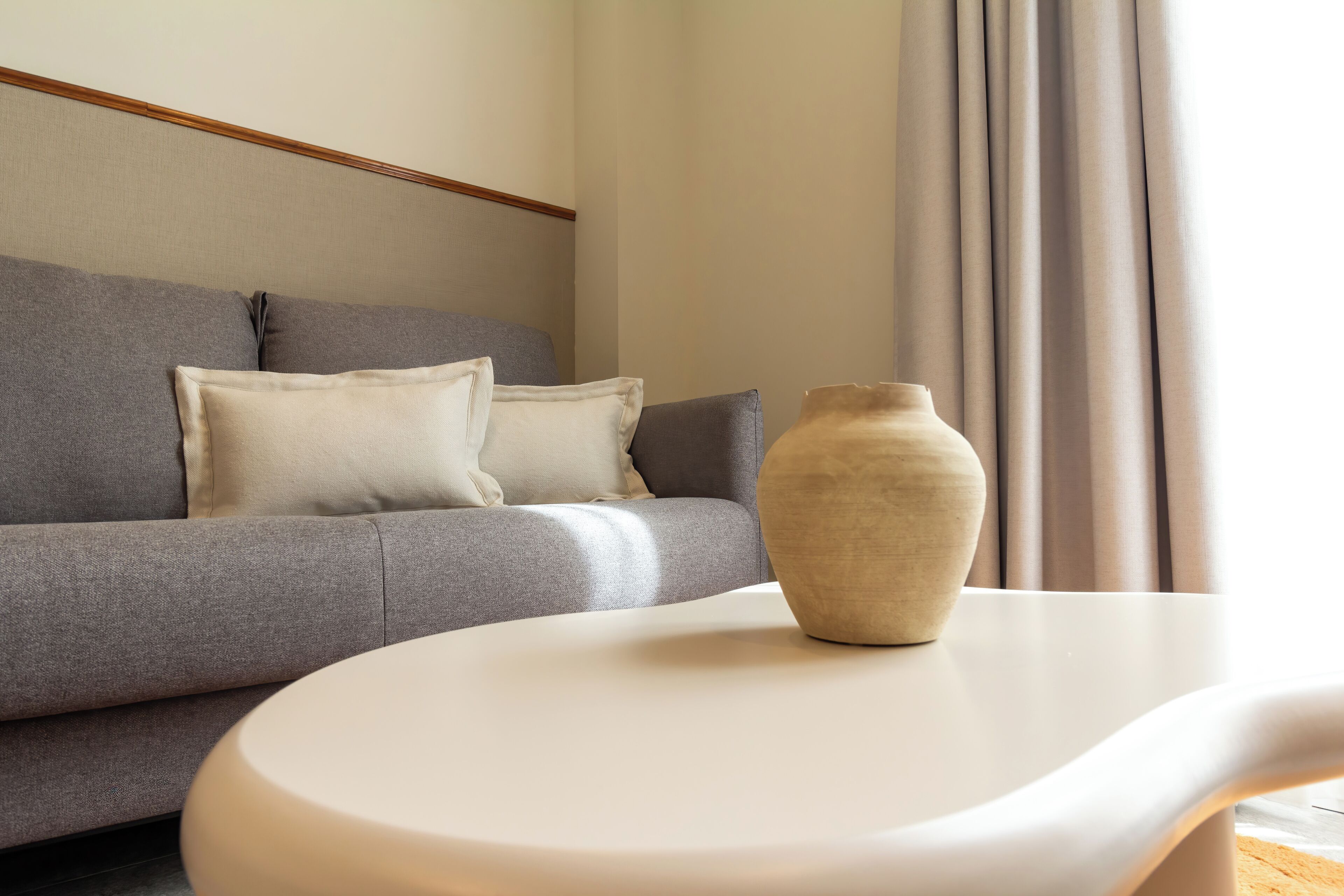 Un salon moderne avec un canapé gris, une table basse blanche et un vase beige.