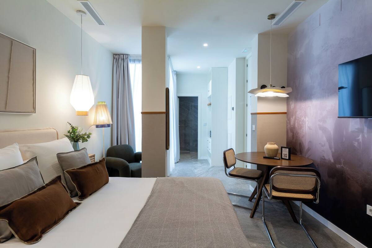 Una camera d'albergo con un letto, una scrivania, sedie, un vaso e una televisione.
