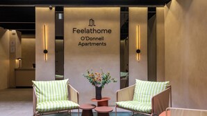 A reception area with a sign for O'Donnell Apartments, two green-striped chairs, a small table, and a vase with flowers. - Feelathome O'Donnell Apartments (Seville)