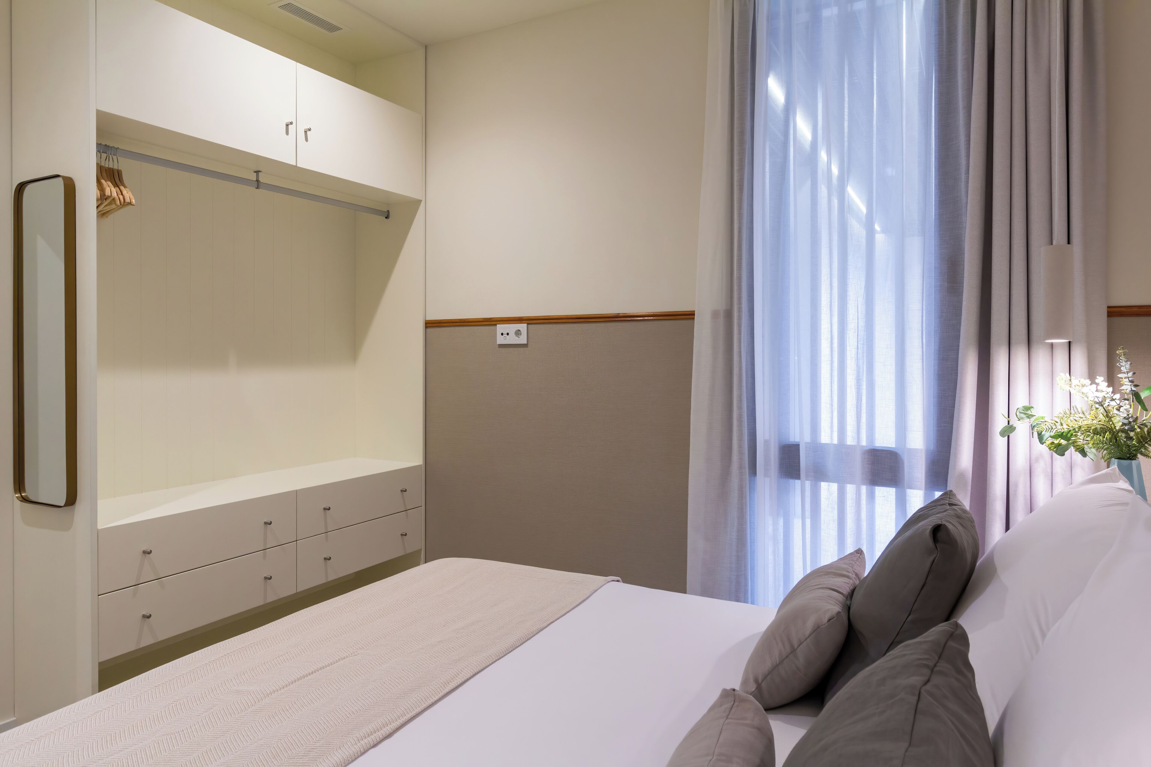 Ett hotellrum med en säng, en garderob och ett fönster med gardiner.