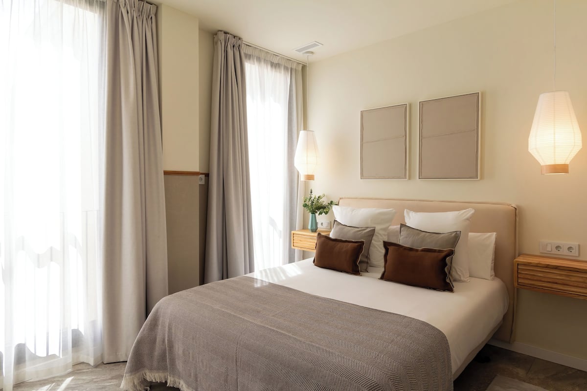 Camera d'albergo con un letto grande, due comodini, una lampada a parete e una finestra con tende.