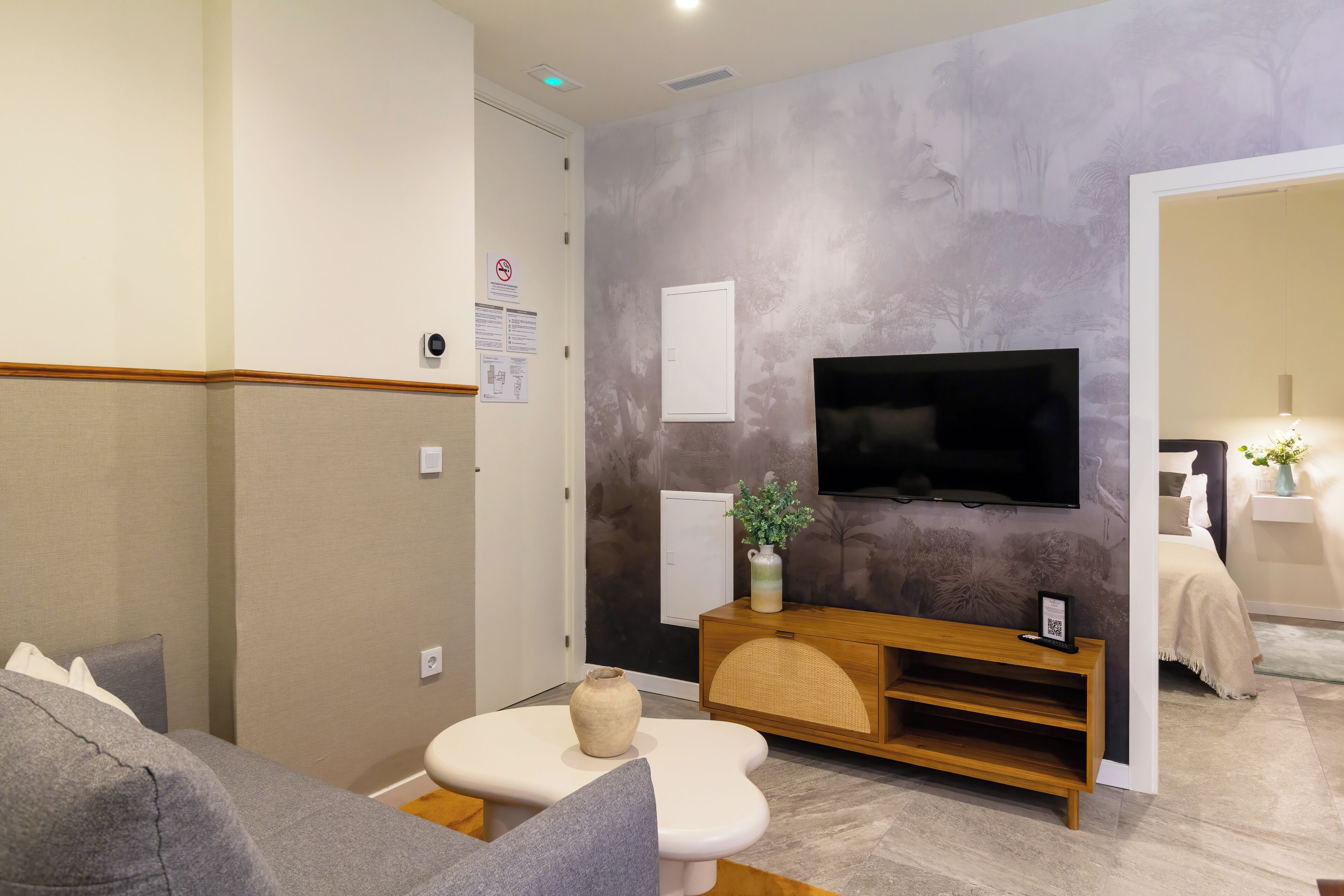 A modern living room with a flat-screen TV mounted on the wall, a wooden console table, a sofa, and a small white table with a vase.