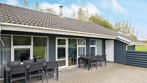 Ein überdachter Patio-Bereich mit Backsteinboden, einem Tisch mit Stühlen und einer Schiebetür zu einem überdachten Außenbereich.