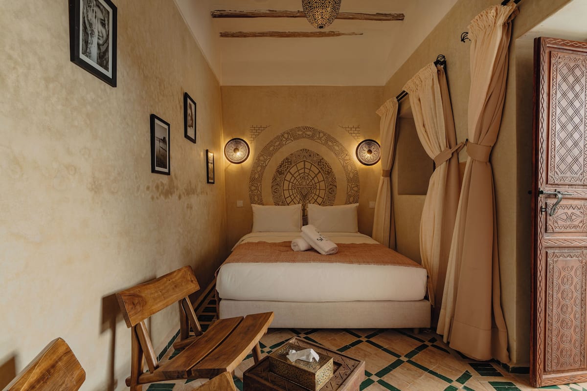 A room with a bed, wooden bench, and a small table.