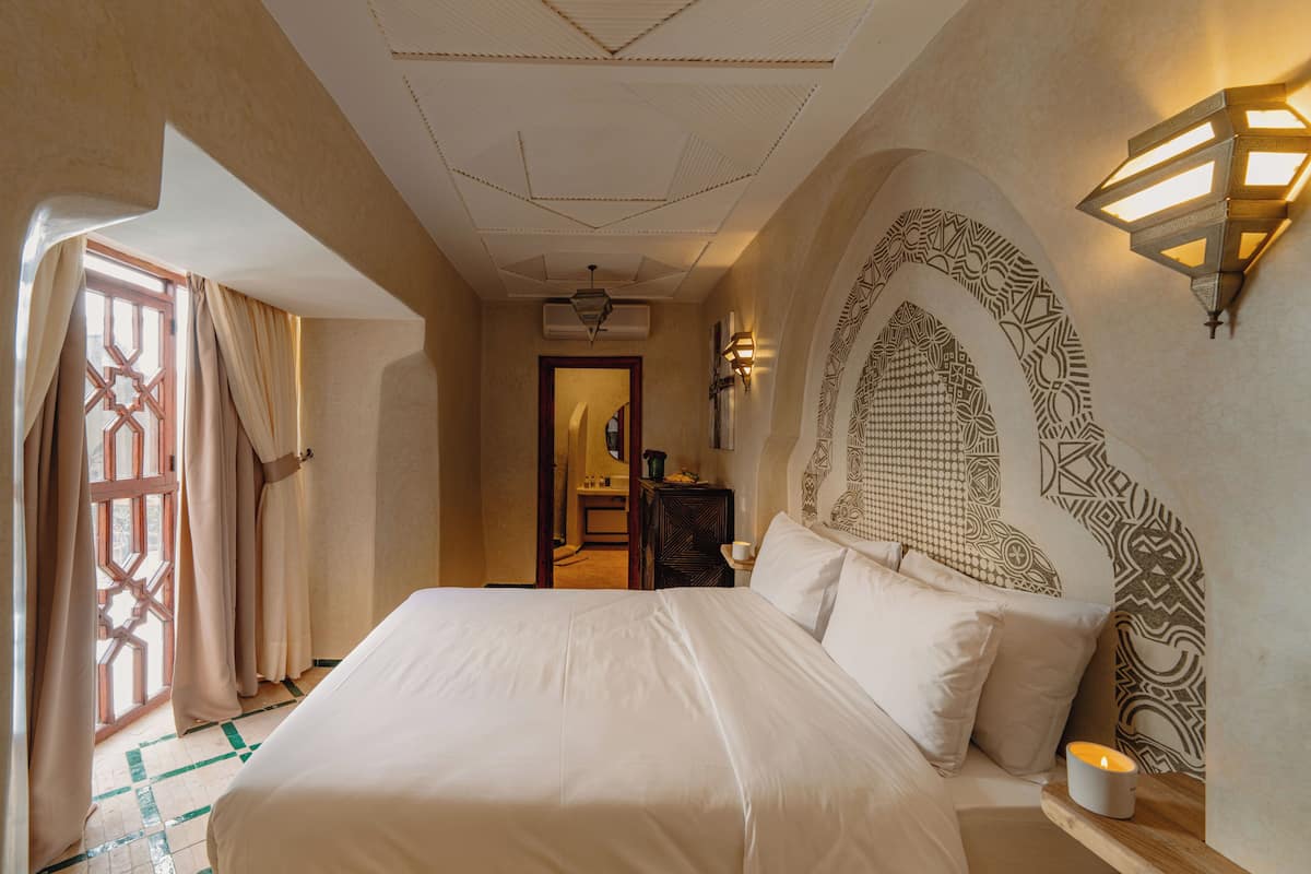 A hotel room with a large bed, a wall-mounted light fixture, and a patterned wall design.
