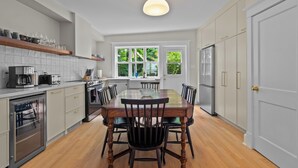 Una cocina moderna con una mesa de comedor de madera, armarios blancos y un amplio ventanal.