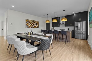 A modern kitchen with dark cabinets, a stainless steel refrigerator, and pendant lighting. - NEW Golfers Dream Modern Patio King Bed (St. John's)