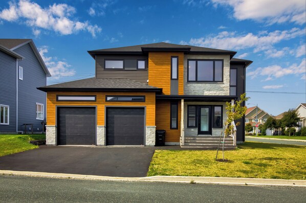 A two-story house with a garage, a stone foundation, and a modern design. - NEW Golfers Dream Modern Patio King Bed (St. John's)