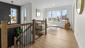 A spacious living area with a wooden staircase, large windows, and a view of the outside. - NEW Golfers Dream Modern Patio King Bed (St. John's)