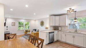 A modern kitchen with white cabinets, a built-in dishwasher, and a window with a view of greenery.