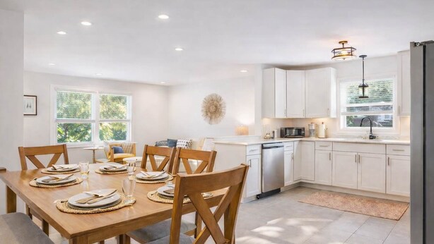 A modern kitchen with white cabinets, a dining table set for six, and a dishwasher.