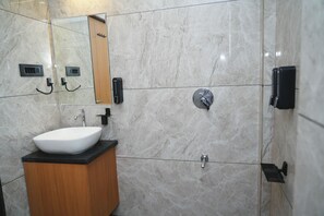 A modern bathroom with a white sink, marble walls, and a mirror. - Hotel Leela's (Dwarka)