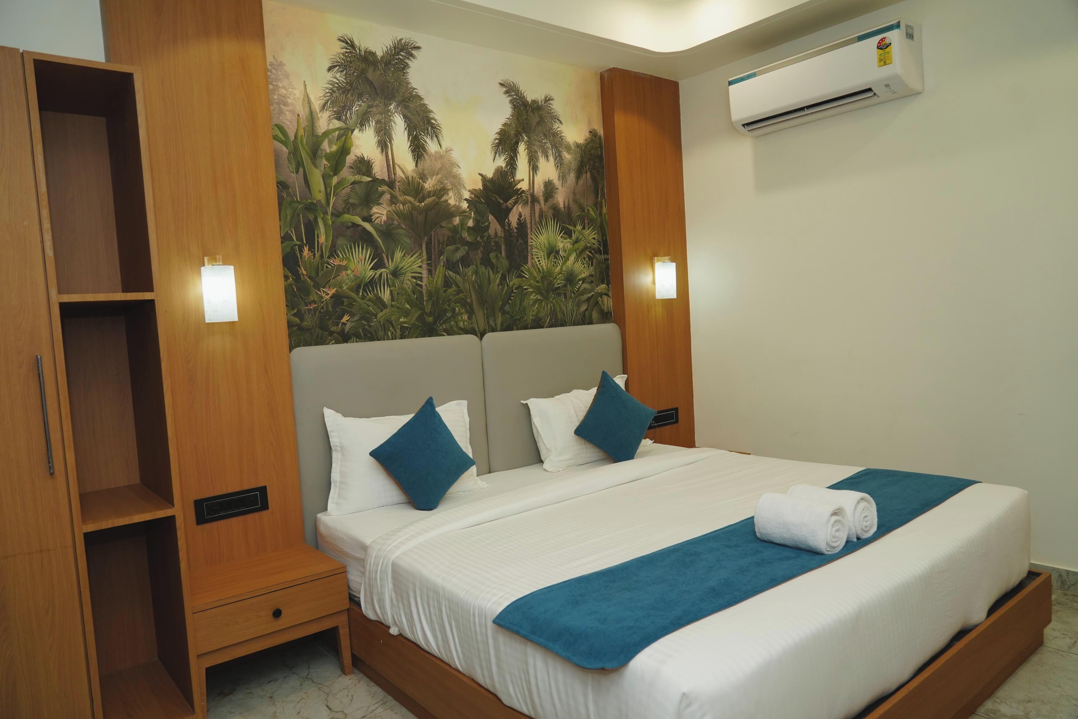 A hotel room with a bed, a wooden wardrobe, a nightstand, and a wall-mounted air conditioner.