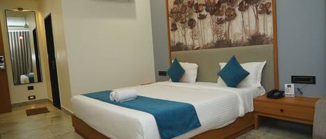 A hotel room with a large bed, a nightstand, an air conditioning unit, and a wall-mounted artwork.