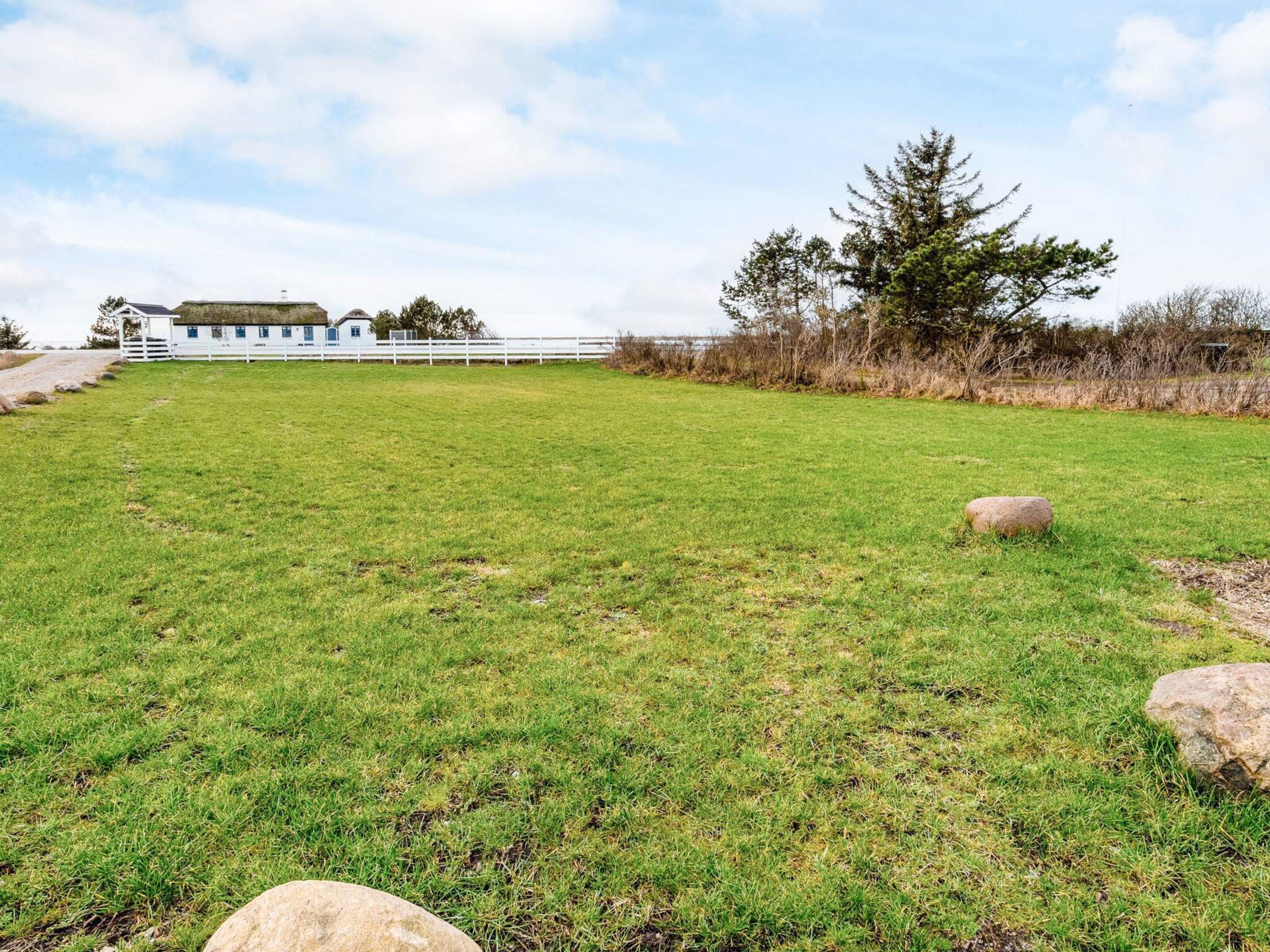 Een grasveld met een witte hek, een grote rots en een gebouw met blauw dak in de verte.