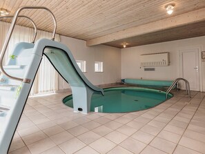An indoor swimming pool with a slide, tiled floor, and a wooden ceiling.