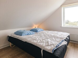 A single bed with a white and blue duvet in a room with a sloped ceiling and a window.