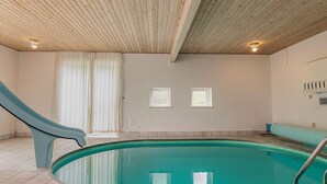 Una piscina interior con techo de madera, suelo de baldosas y dos ventanas.