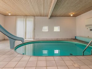 Ein Hallenbad mit Holzbalkendecke, Fliesenboden und zwei Fenstern.