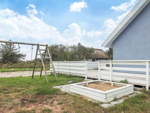 A fenced outdoor area with a swing set and a raised garden bed. - 4 Star Holiday Home in Vestervig (Vestervig)