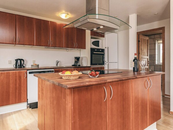 A modern kitchen with wooden cabinets, a central island with fruit, a built-in oven, and a glass-fronted range hood.