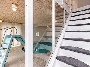 A modern interior with a glass-enclosed swimming pool, a blue slide, and a staircase with black steps.