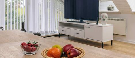 Uma sala de estar moderna com uma mesa de madeira, um cesto de frutas, uma televisão e um armário branco.