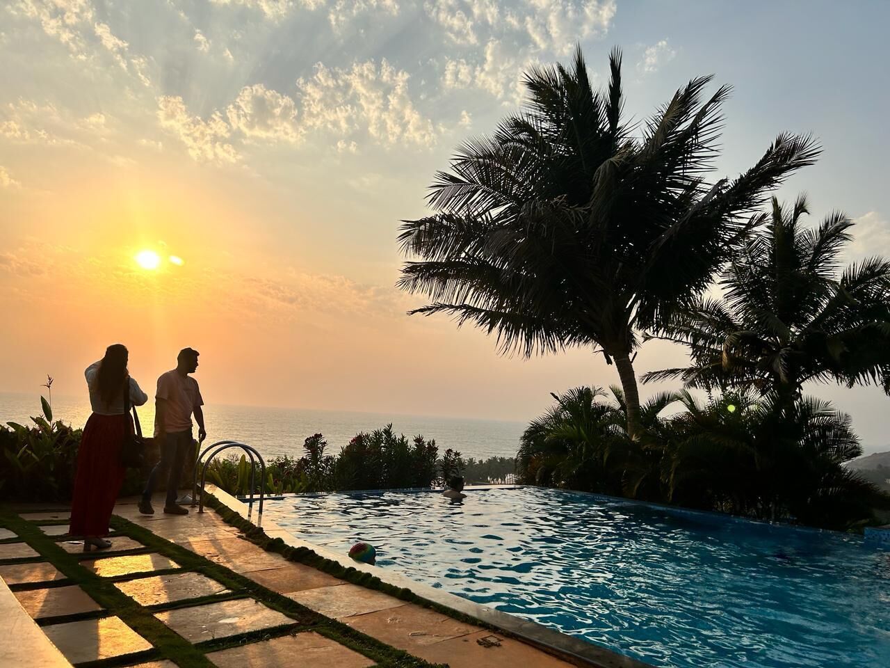 A pool with a view of the sunset and palm trees.