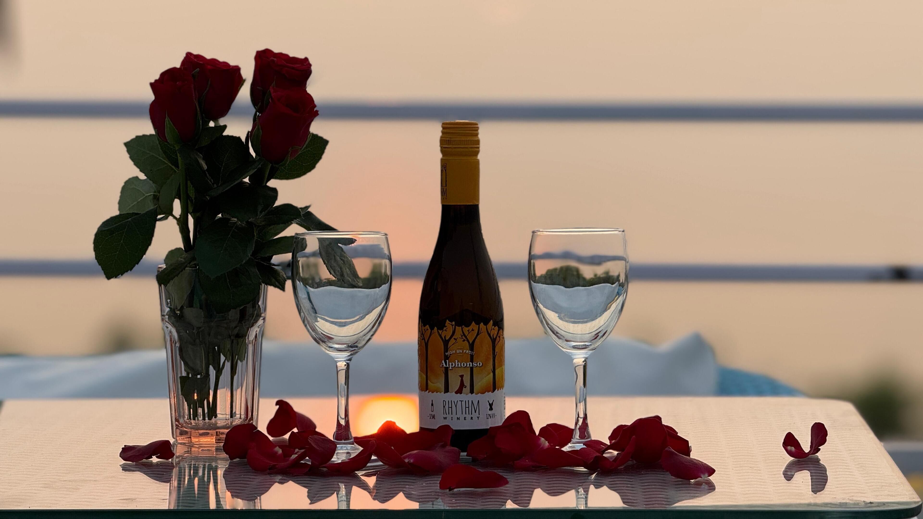 A table with a bottle of wine, two glasses, and a vase of roses.