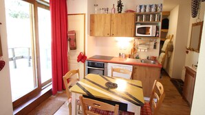 A compact kitchen with wooden cabinets, a microwave, and a dining area with a table and chairs. - Apartment near slopes with terrace (Chamrousse)
