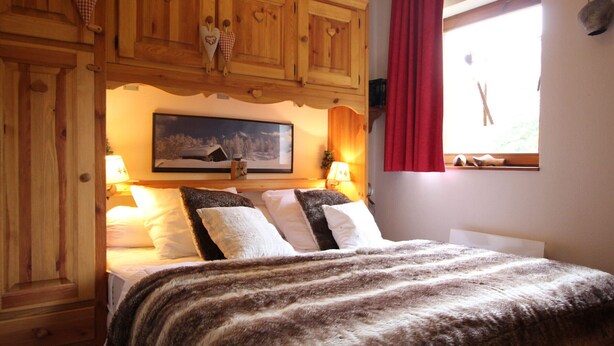 A cozy bedroom with a wooden headboard, a large framed picture, and a window with a red curtain. - Apartment near slopes with terrace (Chamrousse)