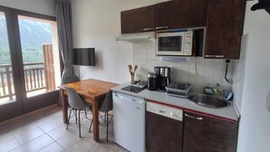 Una cocina compacta equipada con microondas, cafetera y lavavajillas. Hay una mesa de comedor con sillas y un televisor montado en la pared.