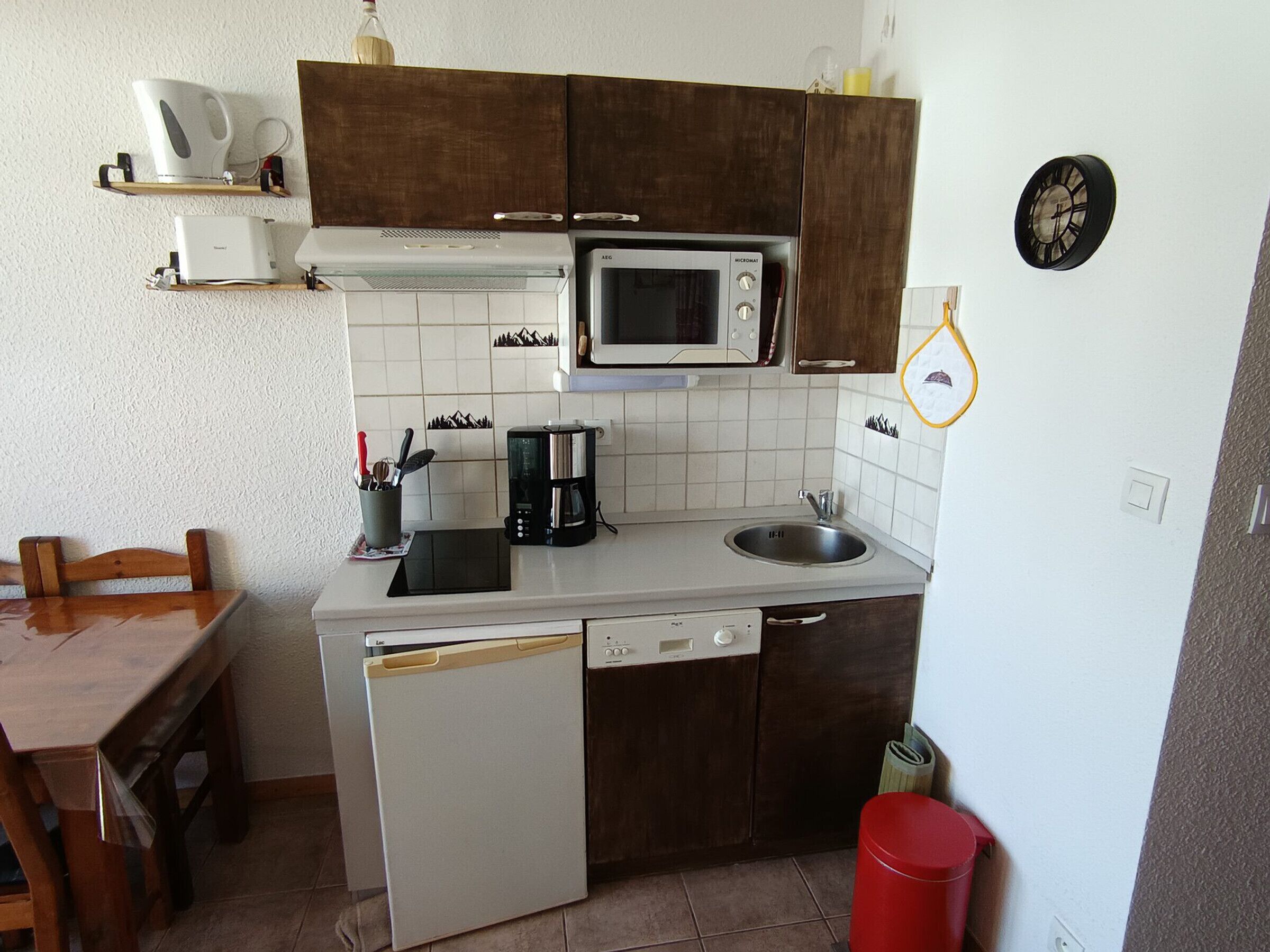 Een compacte keuken met een magnetron, koffiezetapparaat, spoelbak en vaatwasser.