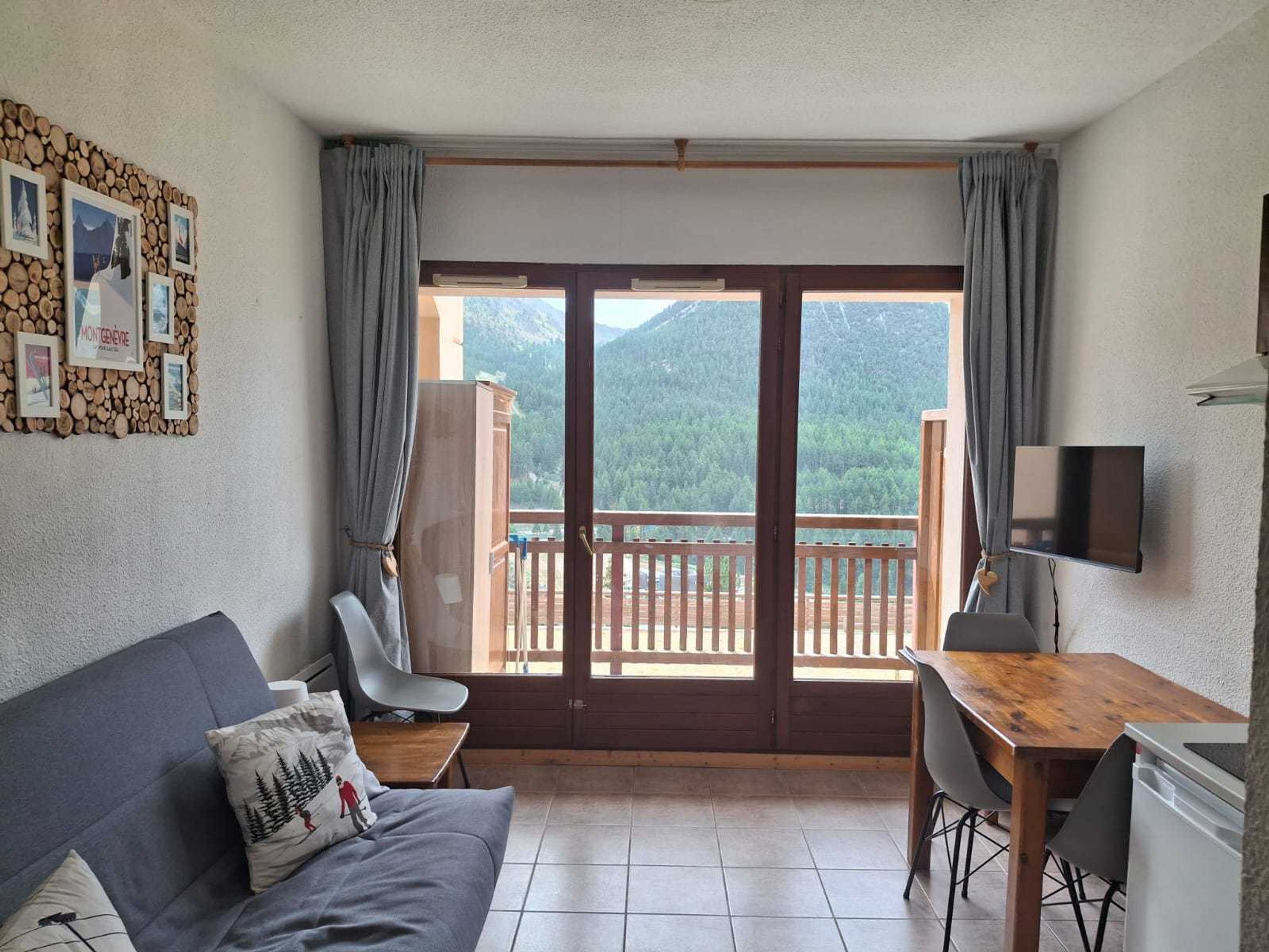 Een kamer met een bank, een bureau, een stoel, een televisie en een balkon met uitzicht op de bergen.