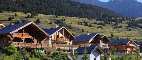 A row of wooden chalets with sloped roofs, set against a backdrop of a mountainous landscape.