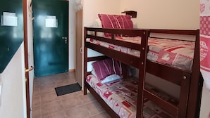 Una cama litera con un edredón estampado, una puerta con picaporte y una lámpara fijada a la pared.