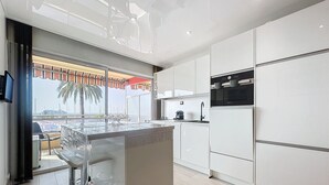 Una cocina moderna con una isla grande, electrodomésticos de acero inoxidable y vistas a una palmera y un edificio a través del ventanal.