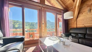 A room with a wooden ceiling, a black leather sofa, a white table with glasses and a tray, and large windows with a mountain view. - Luxury Chalet with Spa & Sauna in Vars (Vars)
