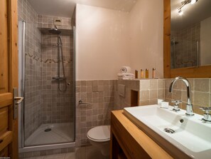 A bathroom with a glass-enclosed shower, a toilet, and a sink with a mirror above it. - Courchevel 1850: 3 Rooms, Balcony, View, Wifi, Garage (Courchevel 1850)